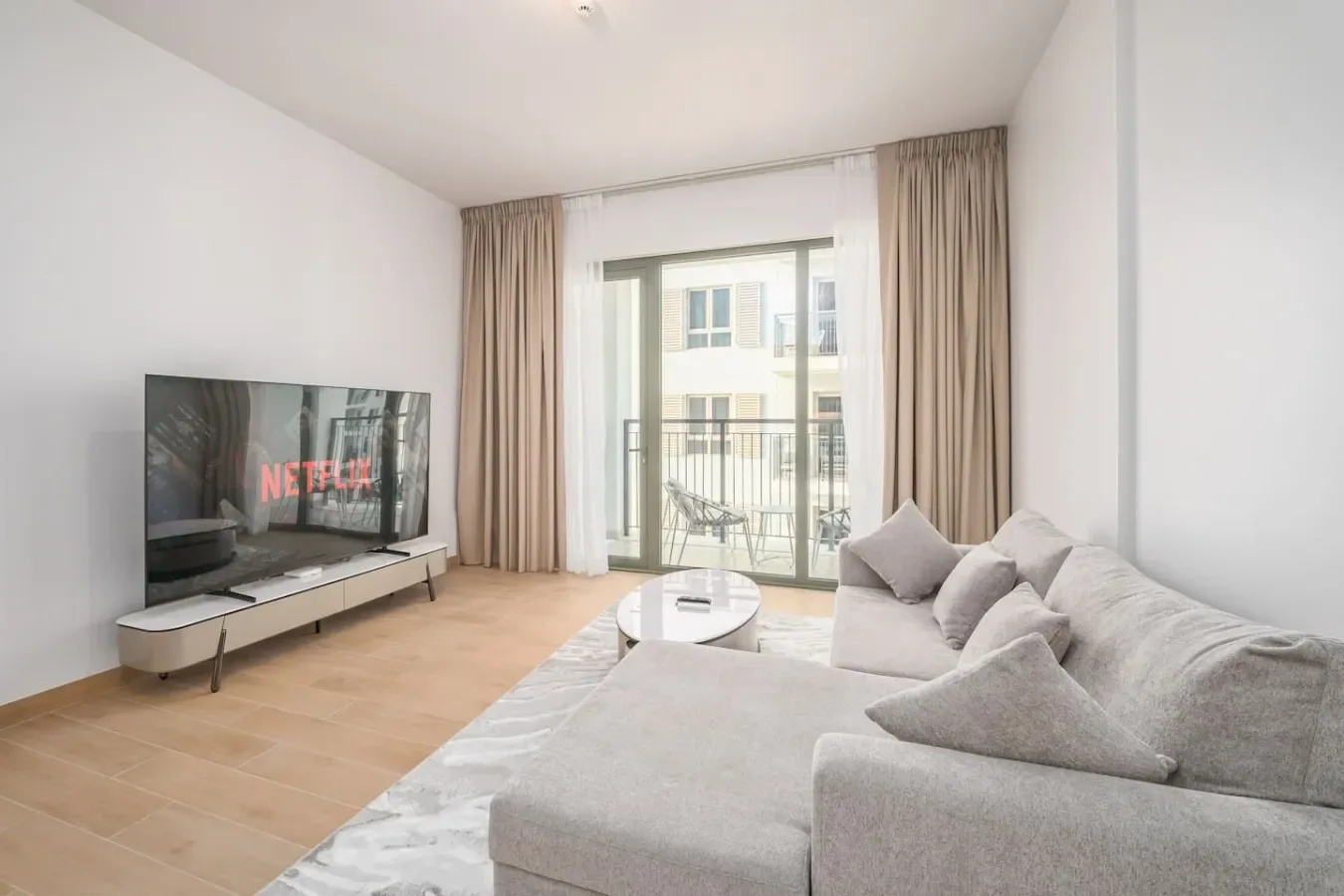 Una sala luminosa con asientos, un televisor y puertas de vidrio que dan a un balcón.