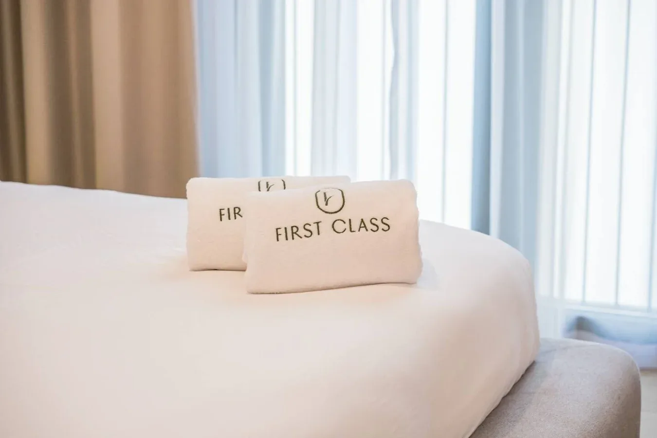 Una cama bien tendida con dos almohadas estampadas frente a cortinas translúcidas.
