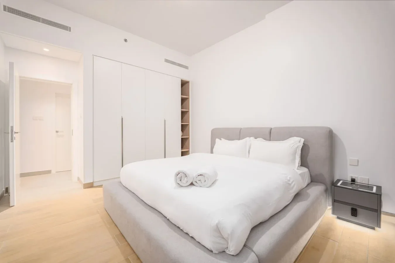 Un dormitorio luminoso con una cama bien tendida y un cabecero tapizado gris.