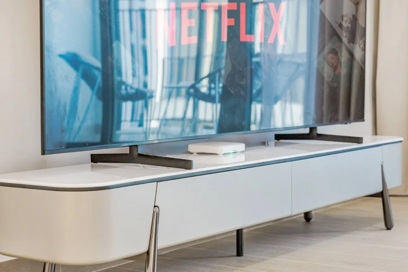 Un televisor con una pantalla de streaming está sobre un largo mueble blanco.