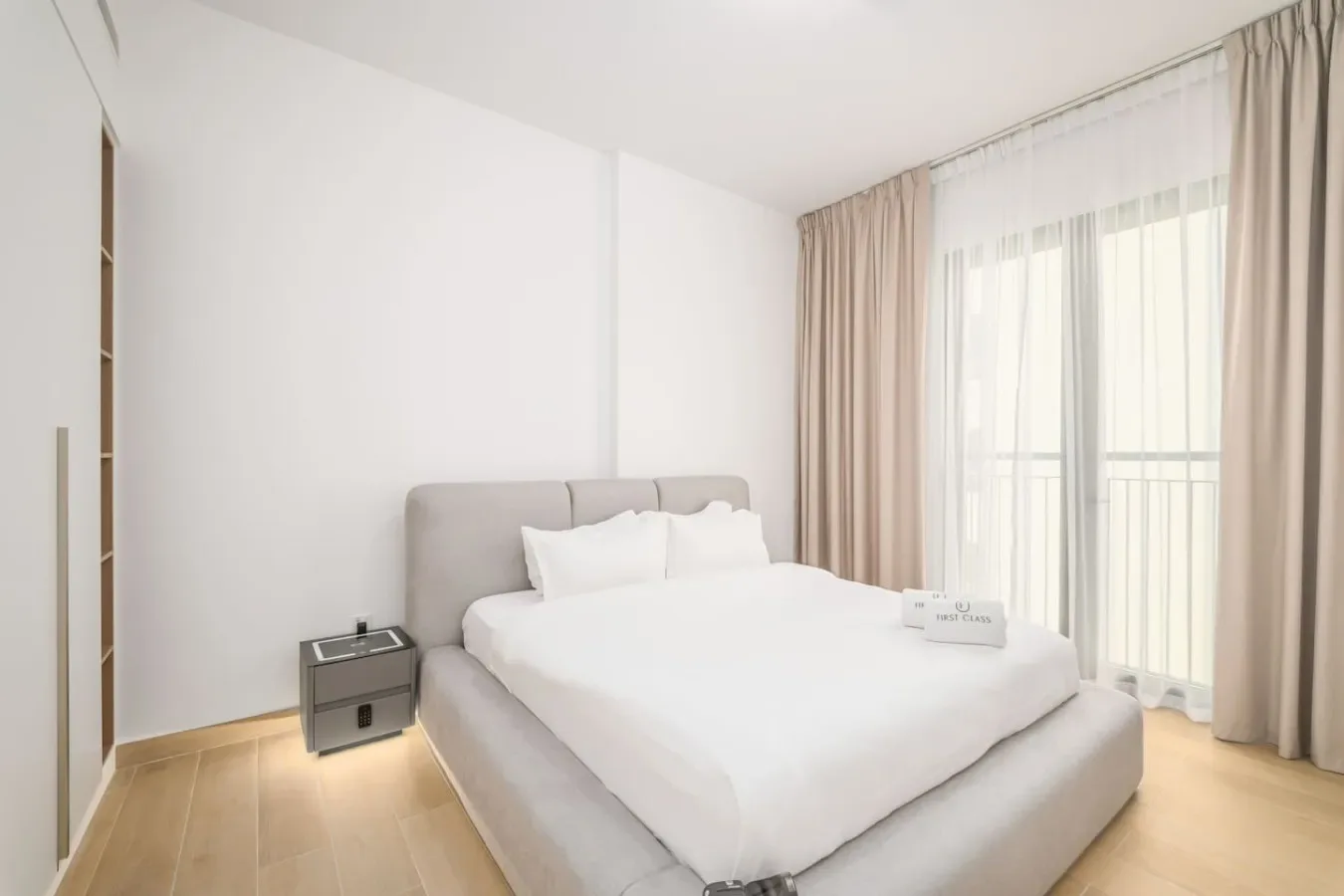 Un dormitorio luminoso con una cama bien tendida junto a altas ventanas con cortinas.