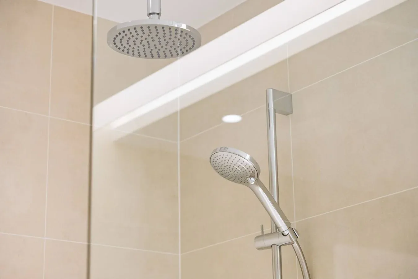 Zona de ducha con azulejos, una ducha de techo y una ducha de mano.