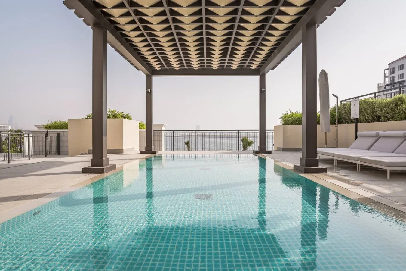 Una piscina bajo una pérgola sombreada, con asientos a un lado.