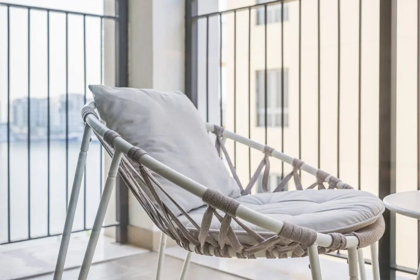 Una silla colgante acolchada está junto a ventanas de piso a techo.