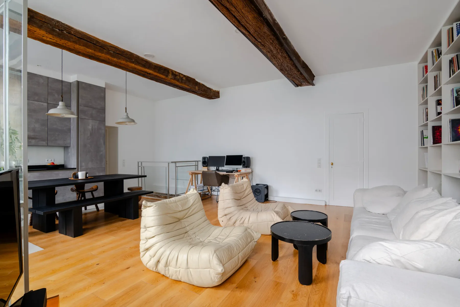 Una sala luminosa con asientos blancos, un escritorio y vigas de madera a la vista.