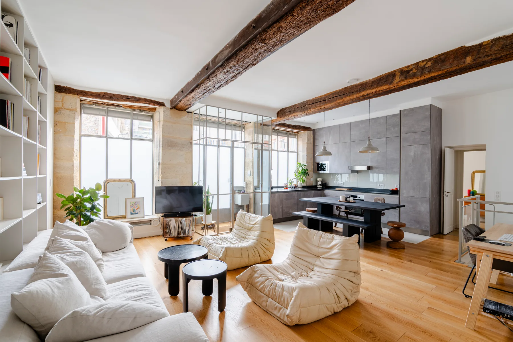 Una luminosa sala de estar diáfana con asientos claros y una cocina al fondo.
