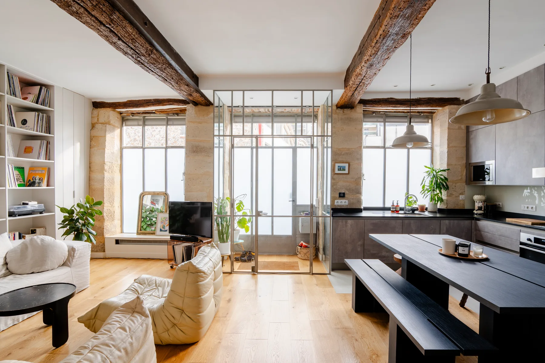 Una sala de estar y cocina de concepto abierto con mesa de comedor y grandes ventanas.
