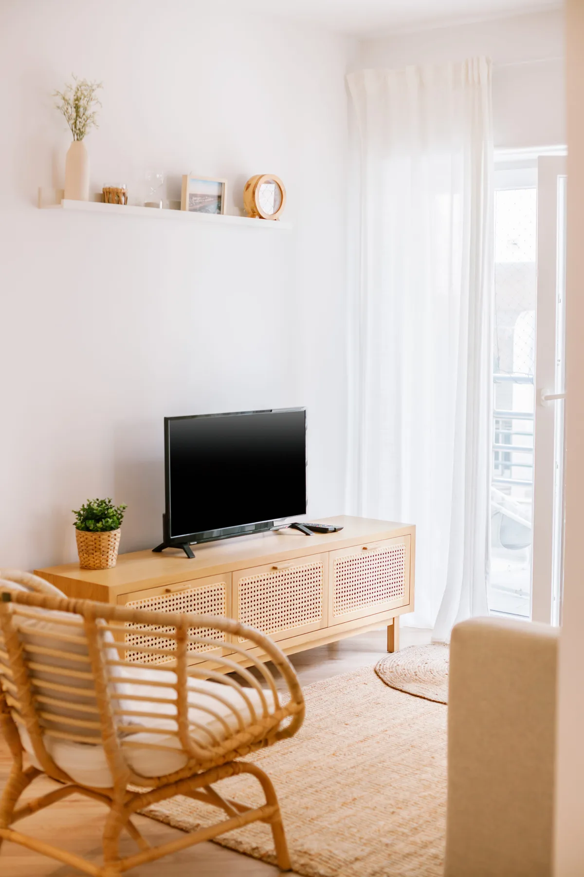 Una sala luminosa con televisor, asientos de mimbre y una puerta de vidrio con cortinas.