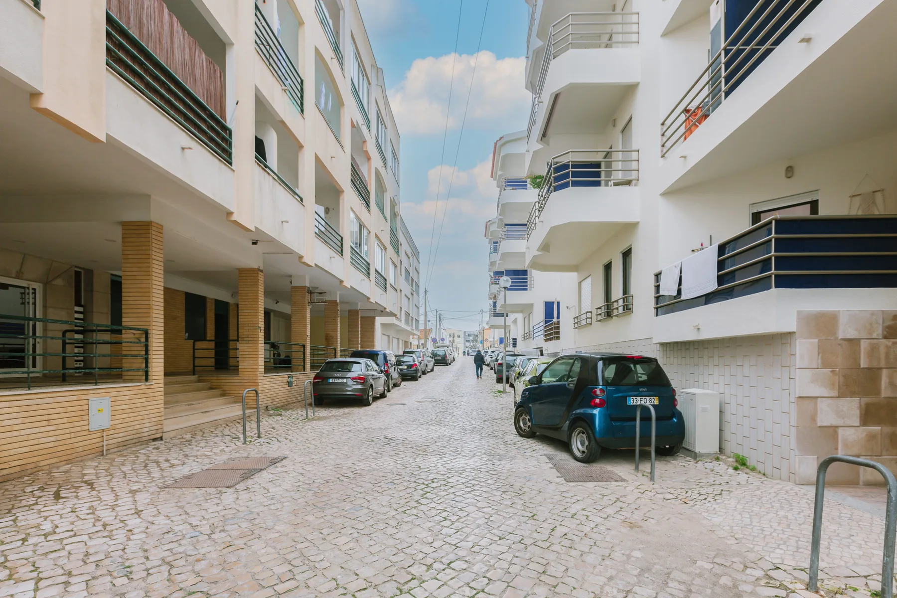 Una calle empedrada pasa entre edificios de apartamentos, con coches aparcados a los lados.