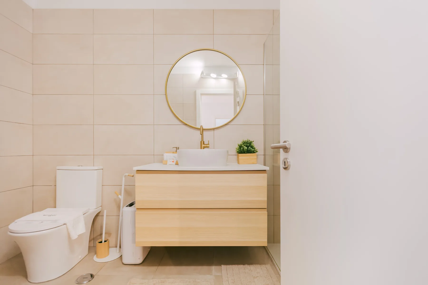 A tiled bathroom with a toilet, vanity, and round mirror.