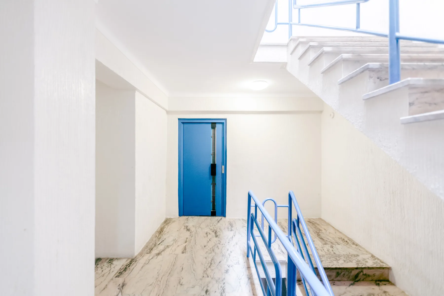 Una escalera interior con barandillas azules y una puerta azul.
