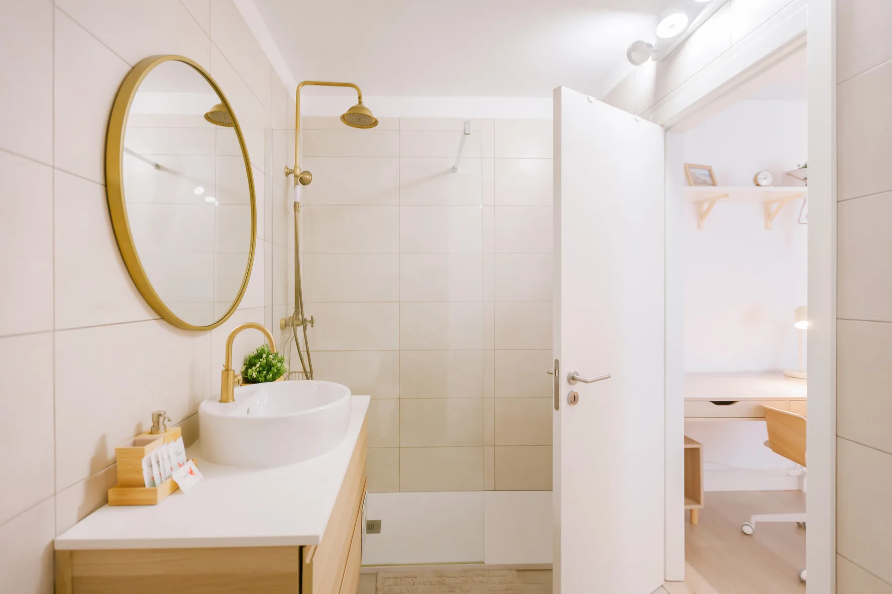 A bright bathroom with a sink, round mirror, and shower.