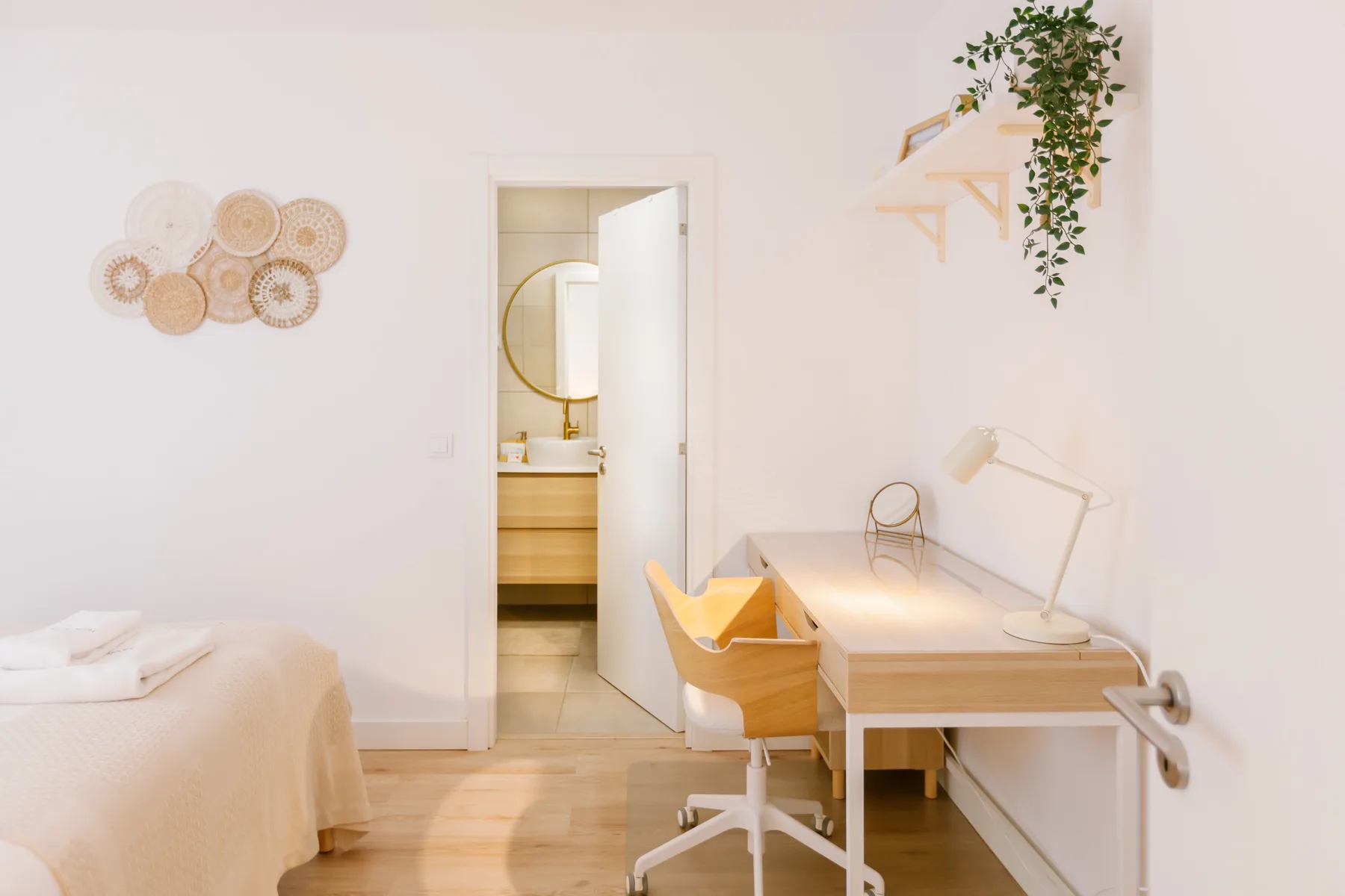 A bright bedroom with a desk and an open doorway to the bathroom.
