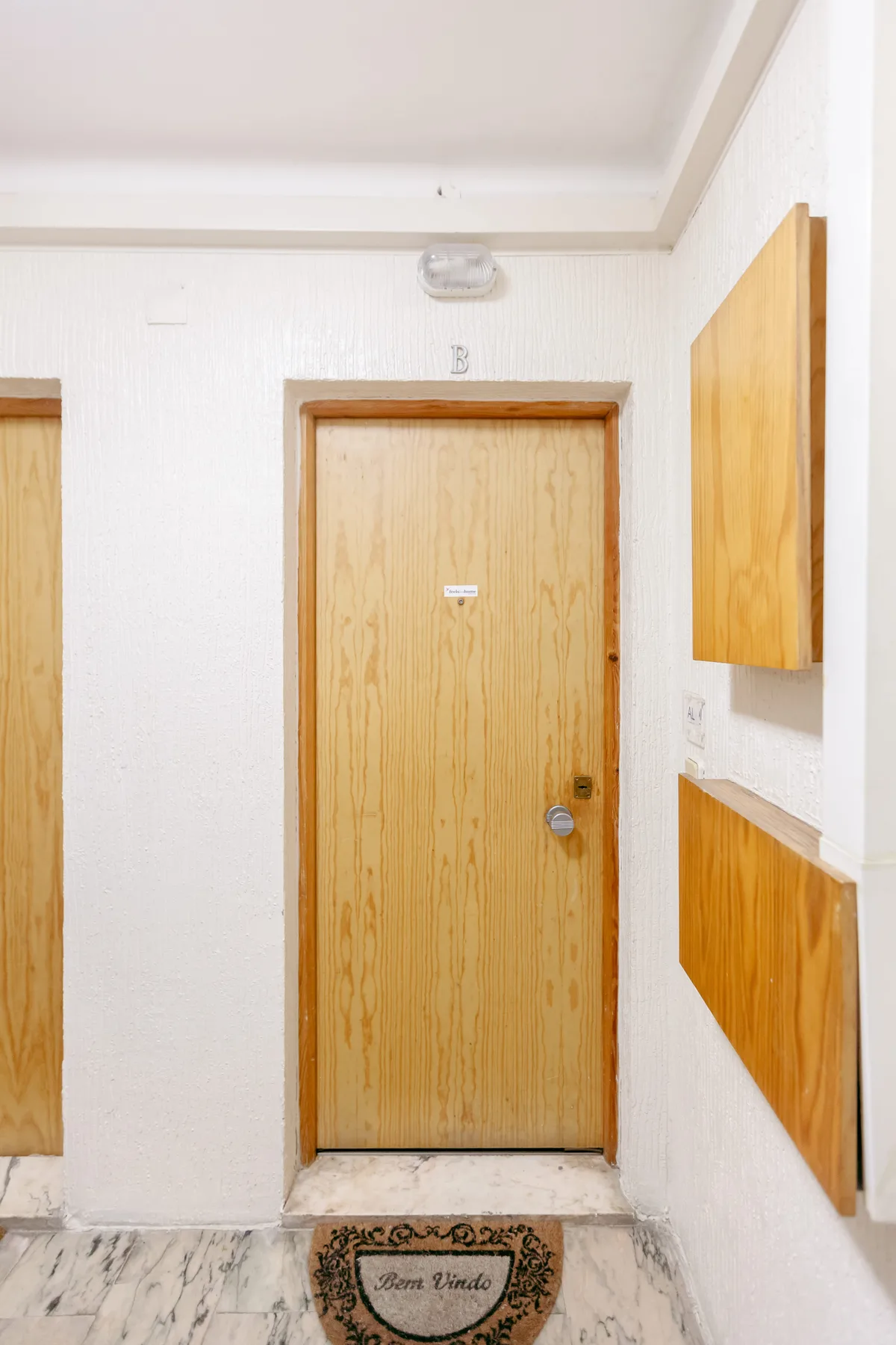 Un pasillo con una puerta de madera y un felpudo de bienvenida.