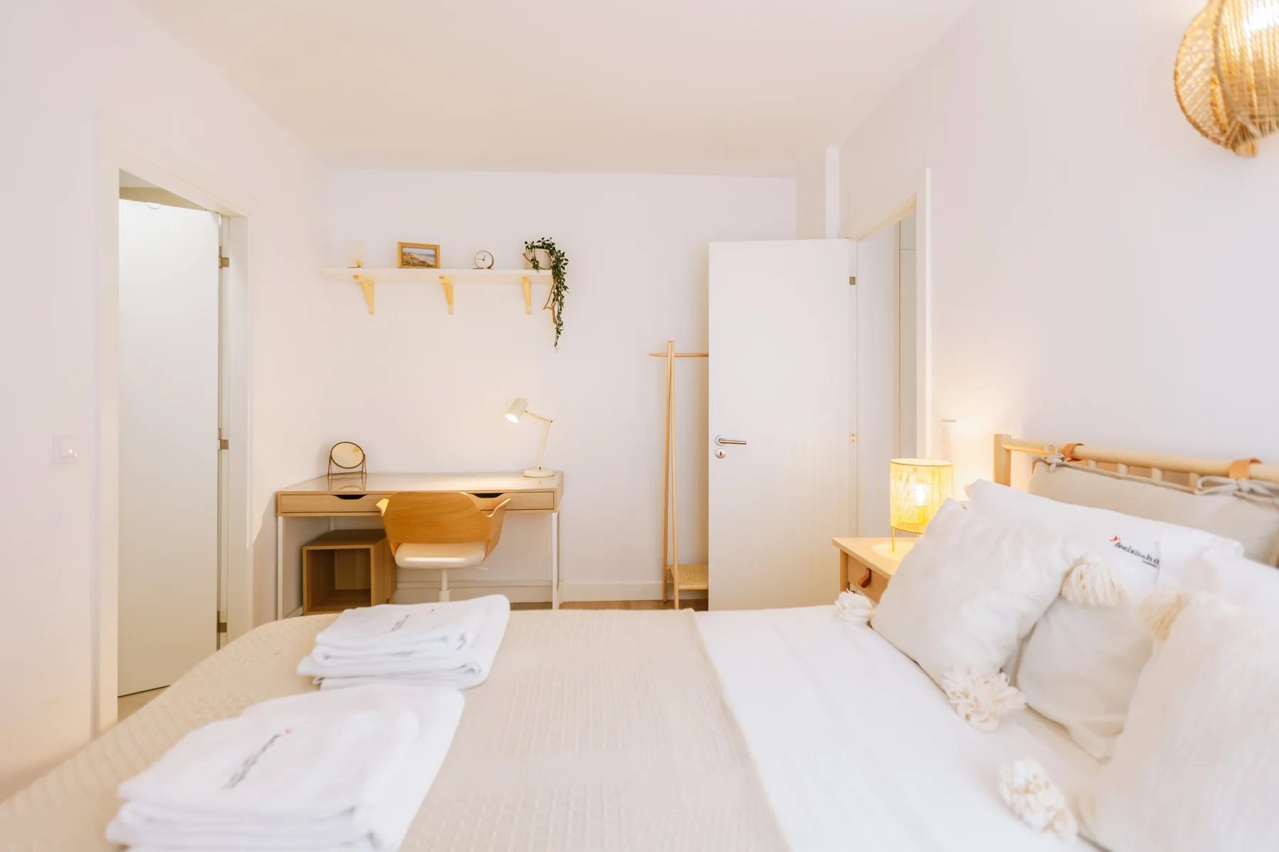 Un dormitorio luminoso con una cama, toallas dobladas y un pequeño estante de pared.
