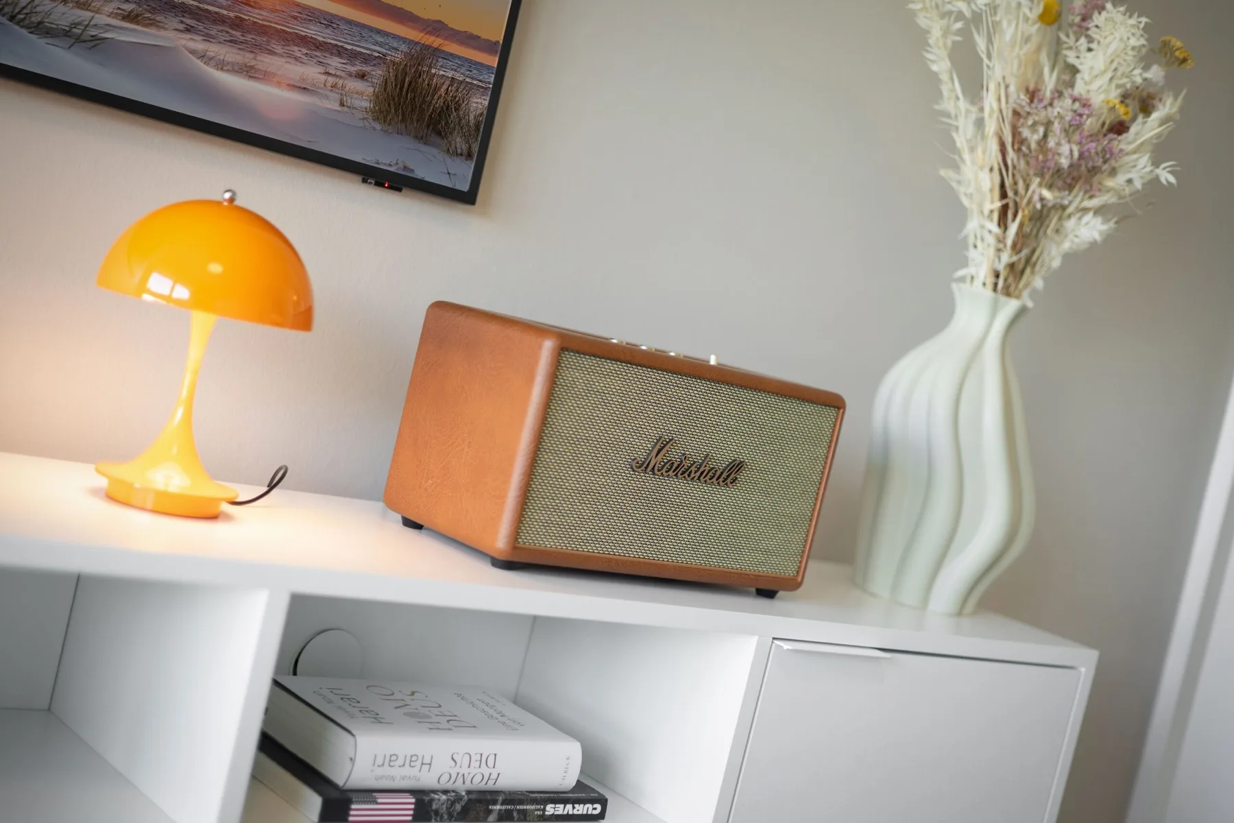 Una consola de sala muestra una lámpara de mesa brillante y un altavoz.
