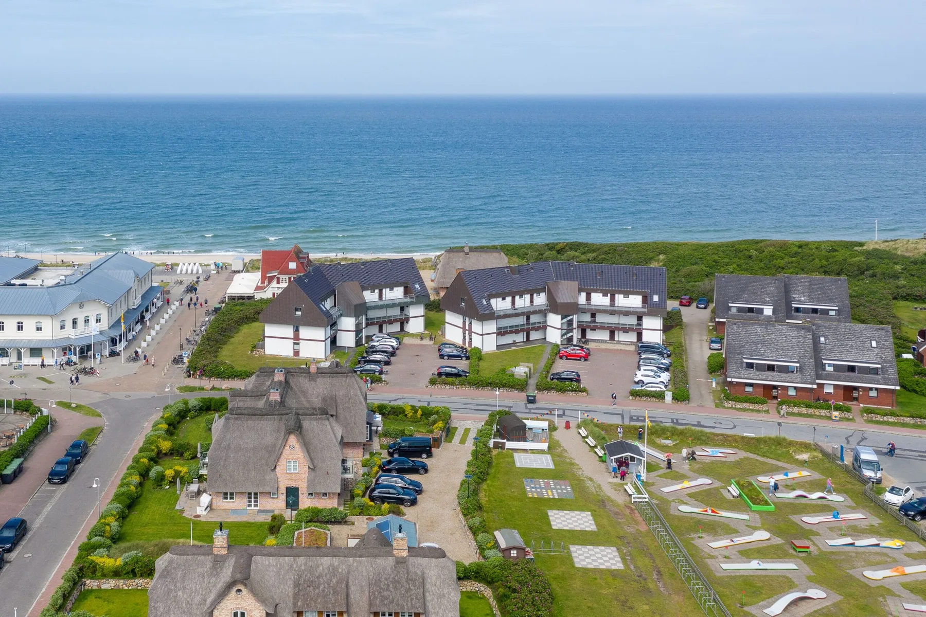 Barrio costero junto al mar, con viviendas y una zona exterior ajardinada.