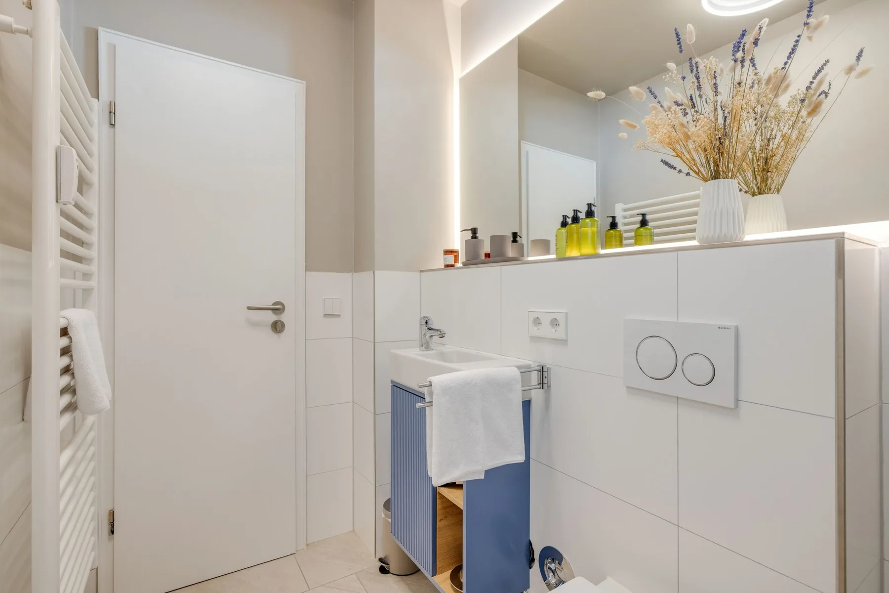 Un baño luminoso con lavabo, espejo de pared y paredes de azulejos blancos.