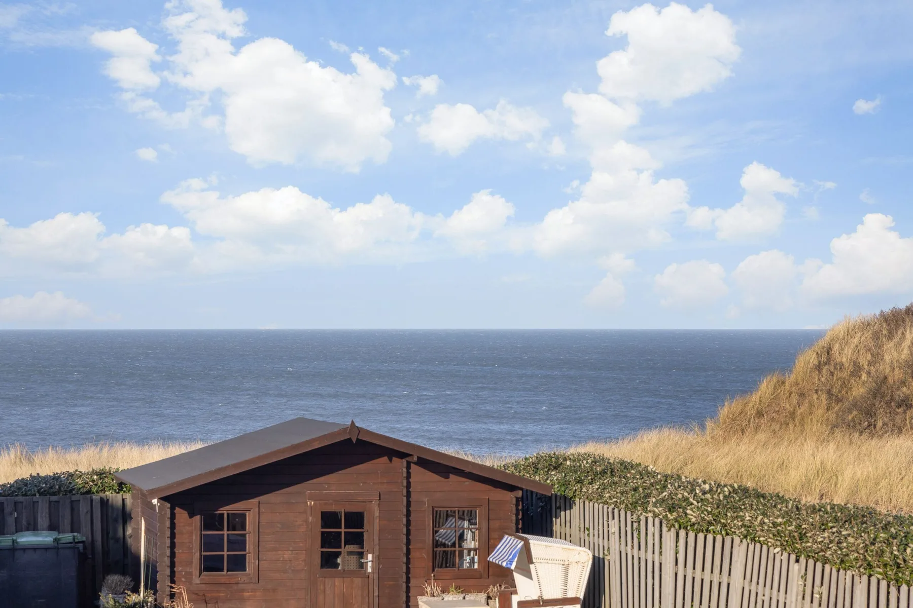 Una pequeña cabaña de madera está junto a la costa, con el océano al fondo.