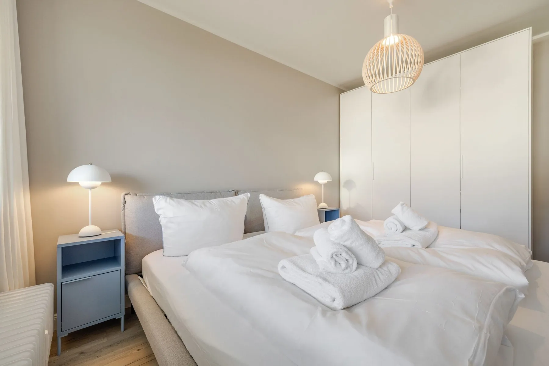 Un dormitorio luminoso con ropa de cama blanca y toallas dobladas sobre las camas.