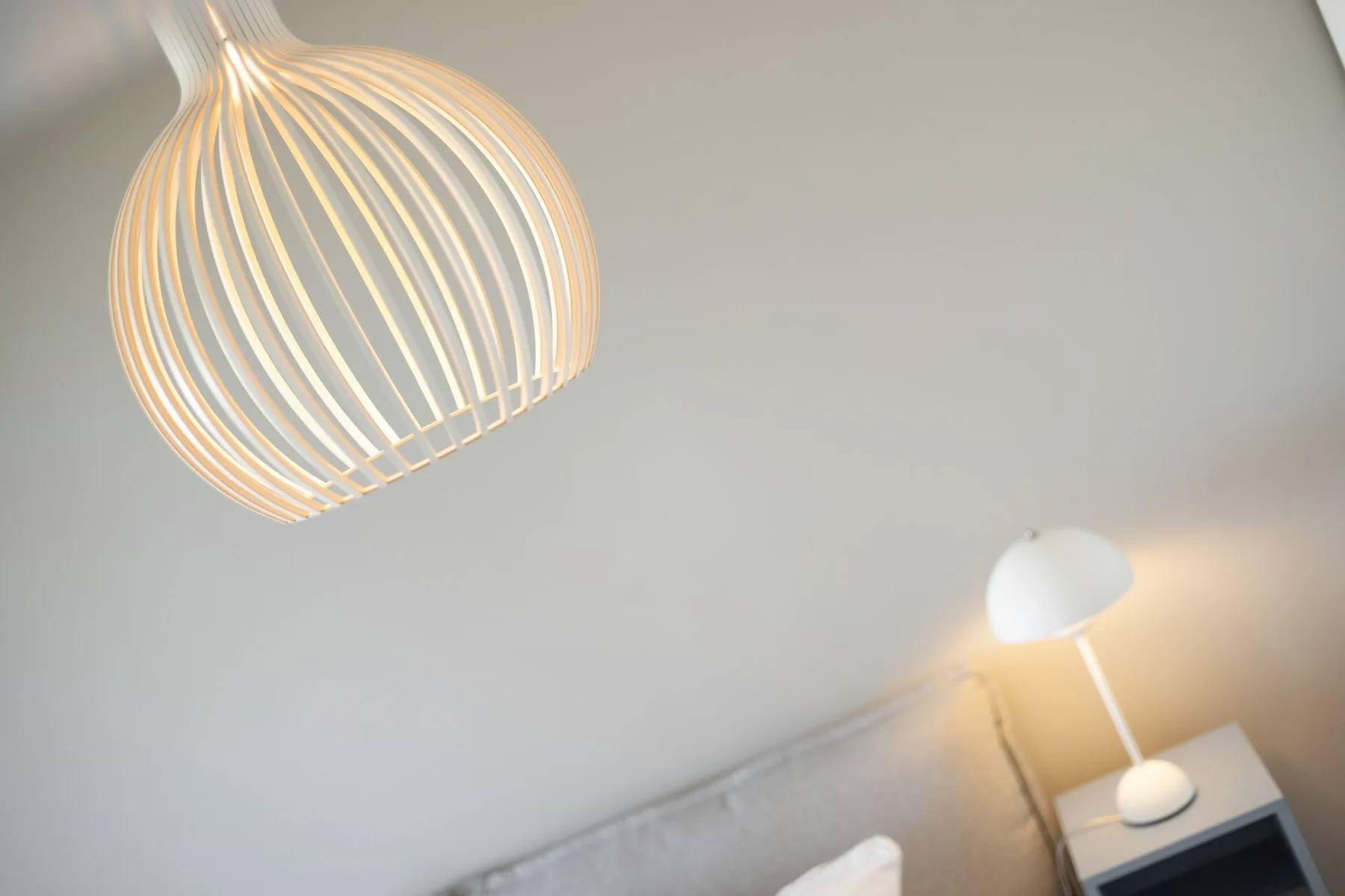 Dos lámparas colgantes iluminan un techo claro y la esquina de una habitación.