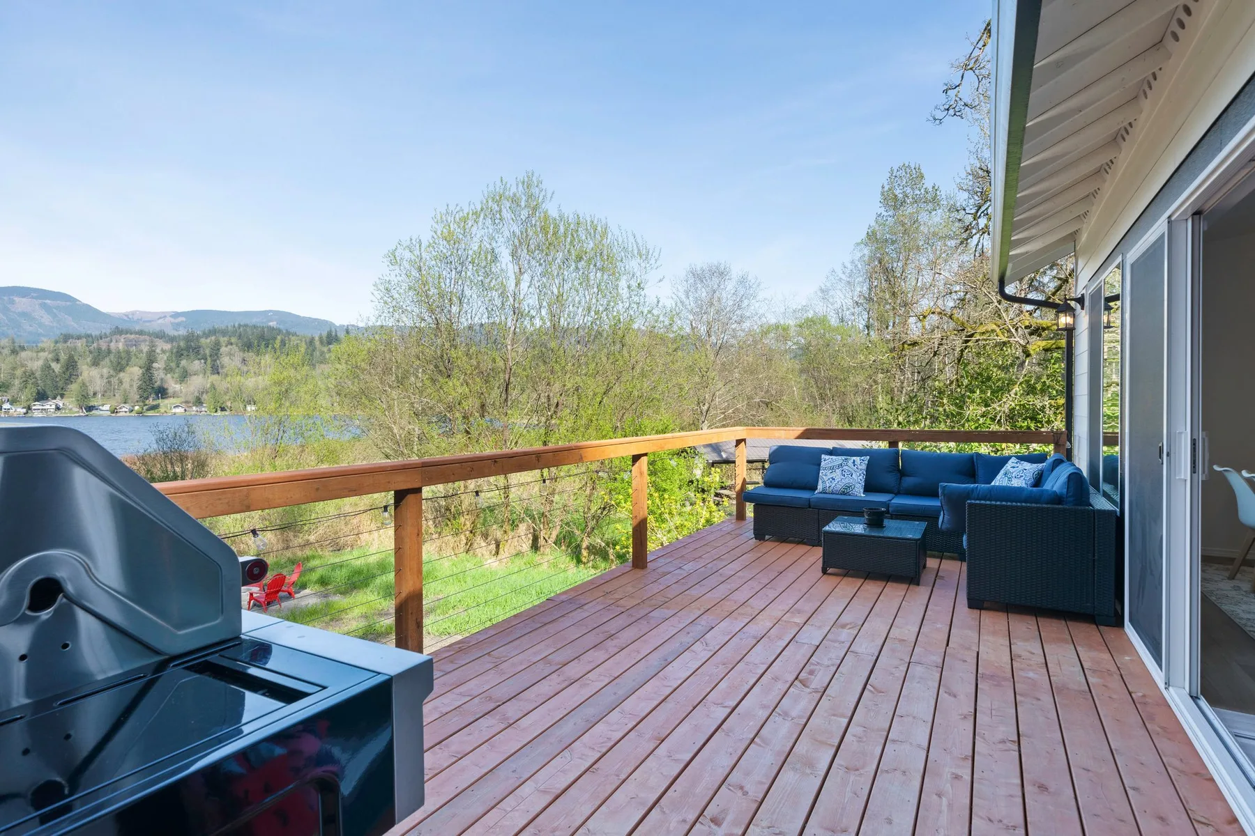 Una terraza de madera con asientos al aire libre da a un lago y colinas boscosas.
