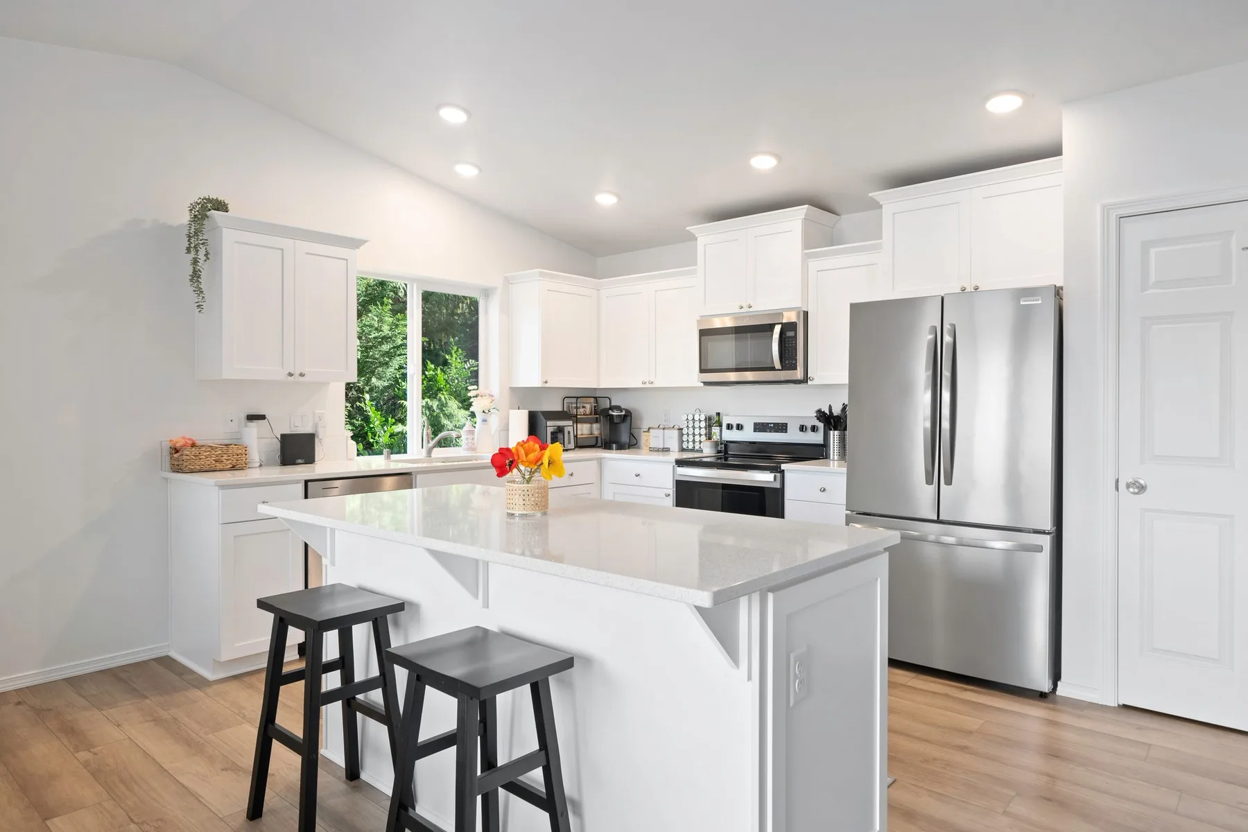 Una cocina luminosa con gabinetes blancos, electrodomésticos de acero inoxidable y una isla central.