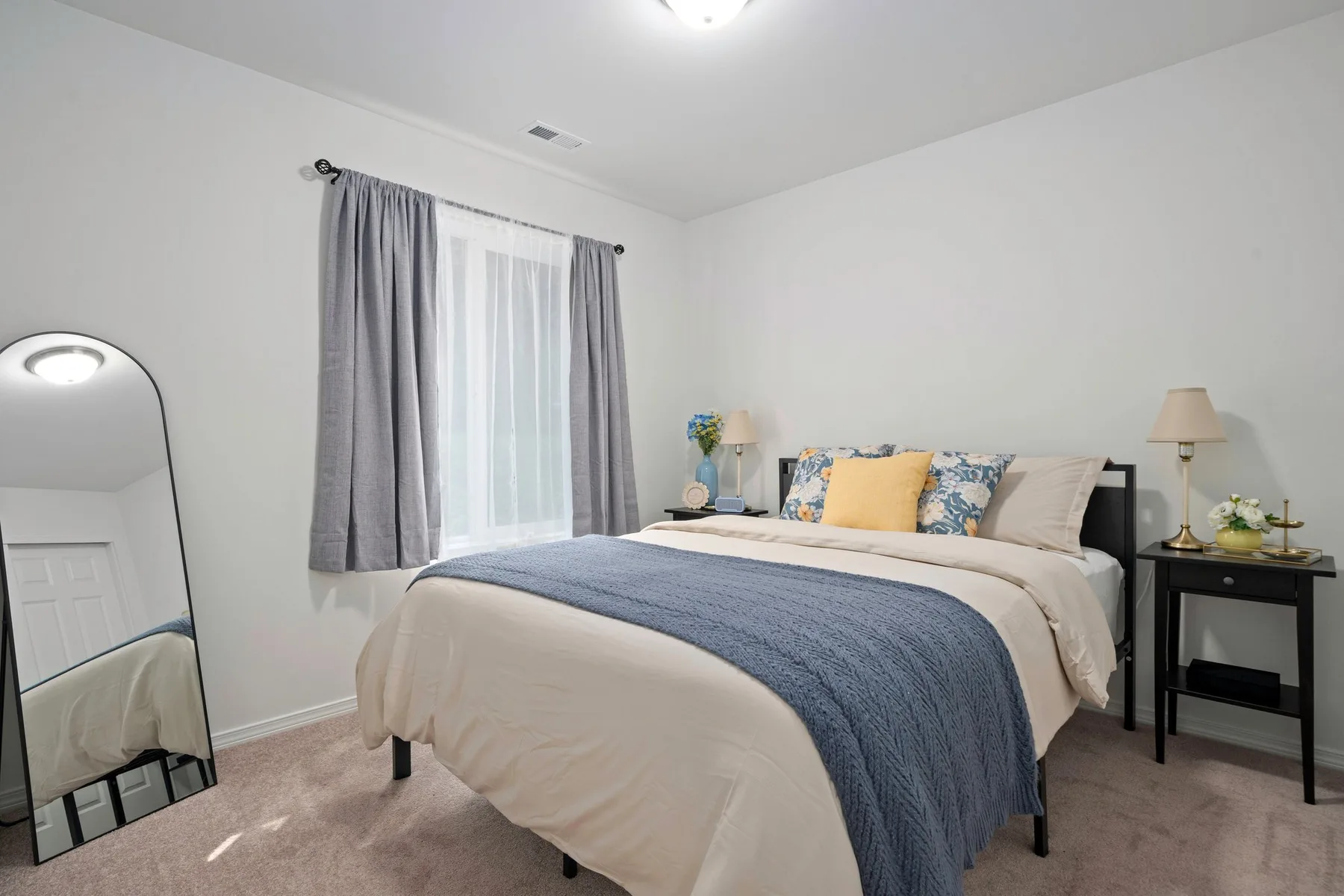 Un dormitorio con una cama vestida con ropa clara y una manta azul junto a una ventana.