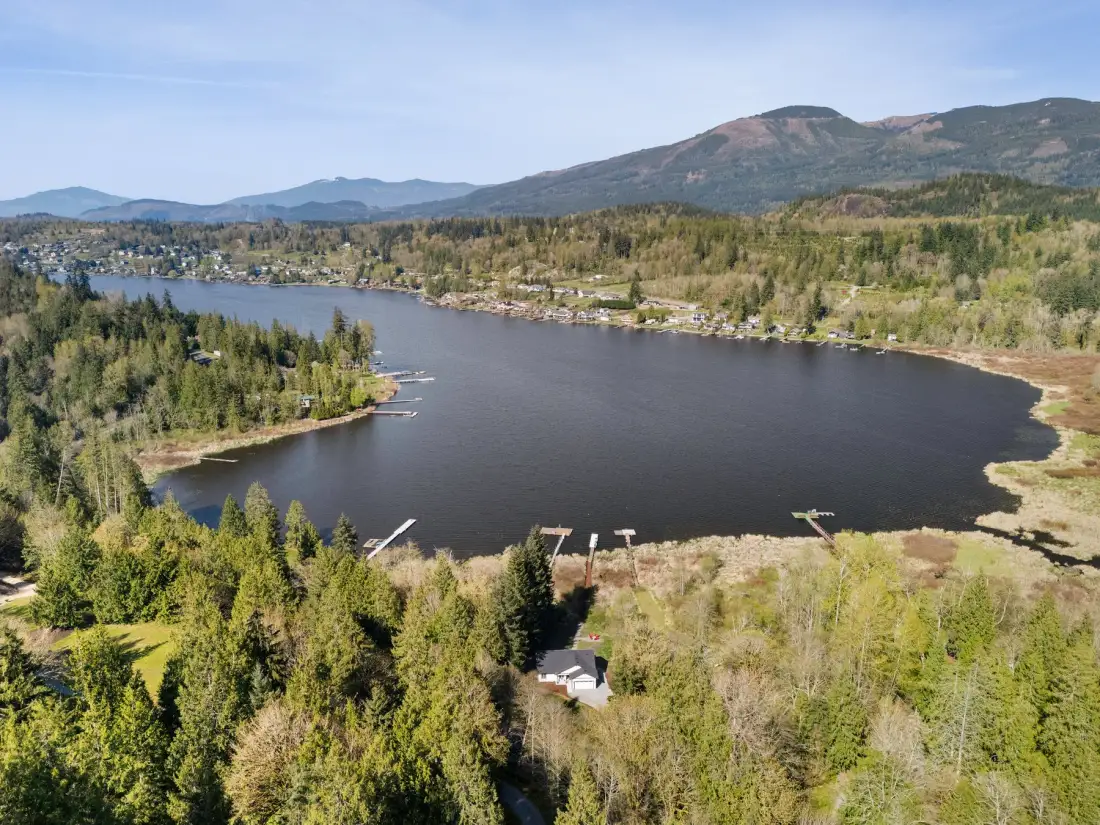 Vista aérea de un lago rodeado de bosque, con montañas a lo lejos.