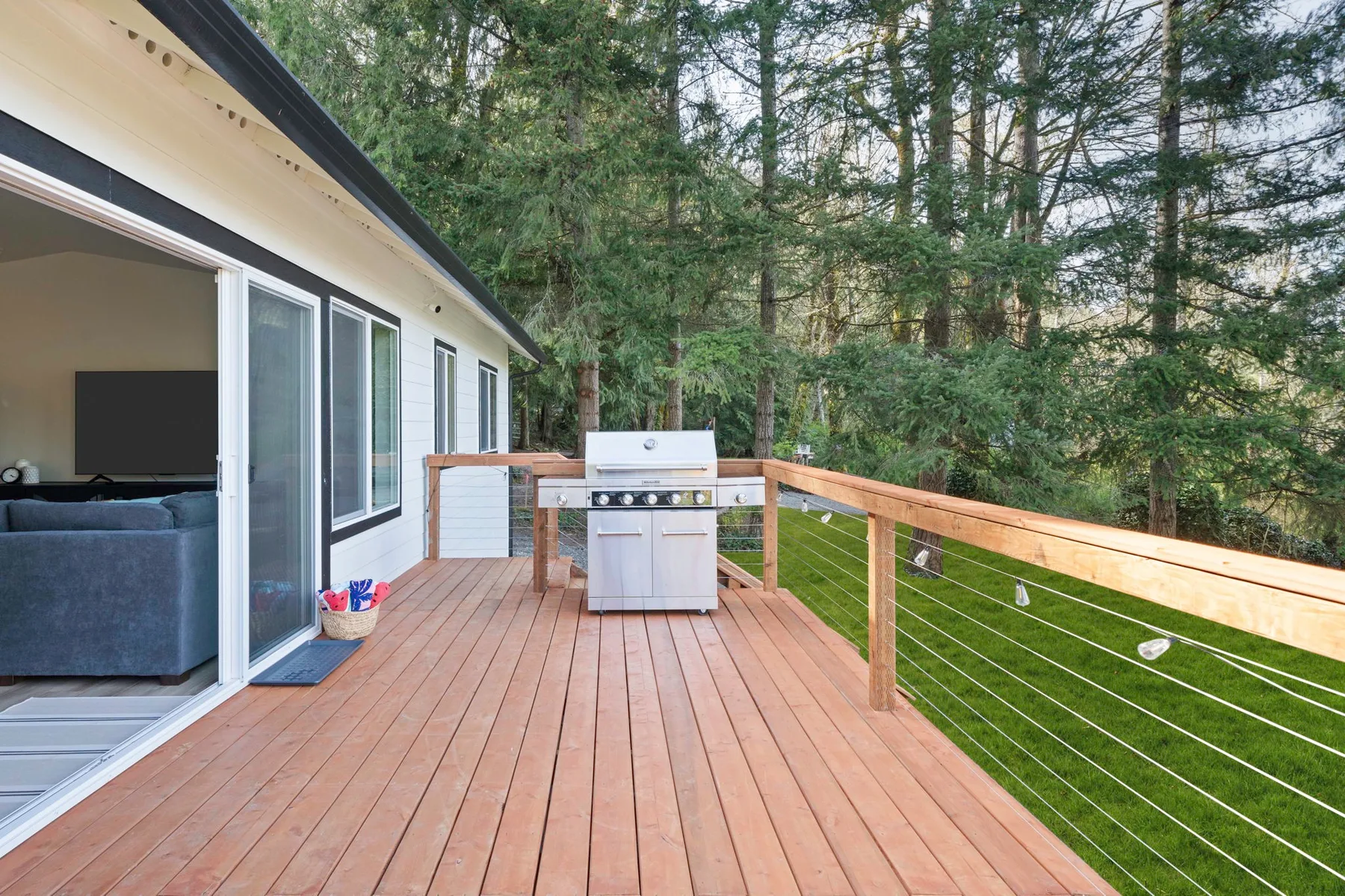 Una terraza de madera con una parrilla da a un jardín verde y árboles.
