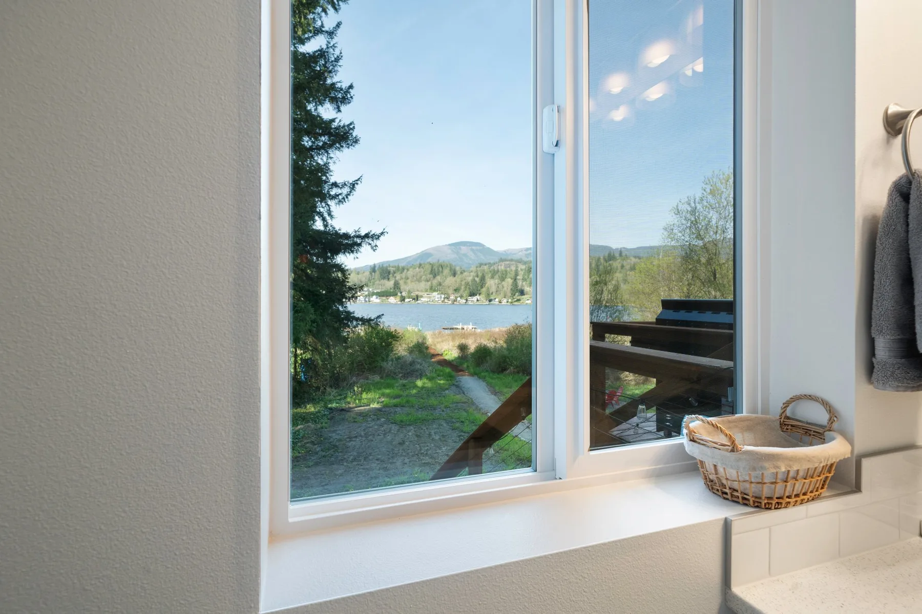 Una ventana amplia da a un lago, una orilla verde y colinas lejanas.