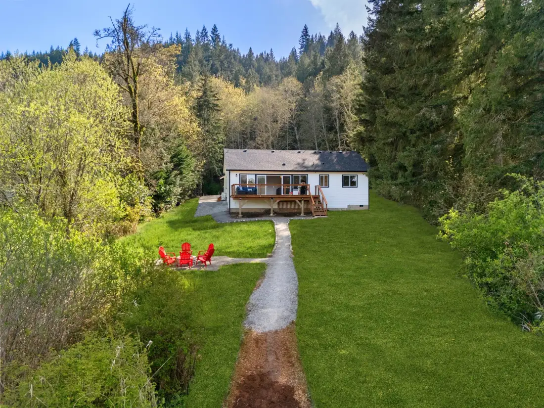 Una casa pequeña está junto a un sendero en un claro con césped rodeado de árboles.