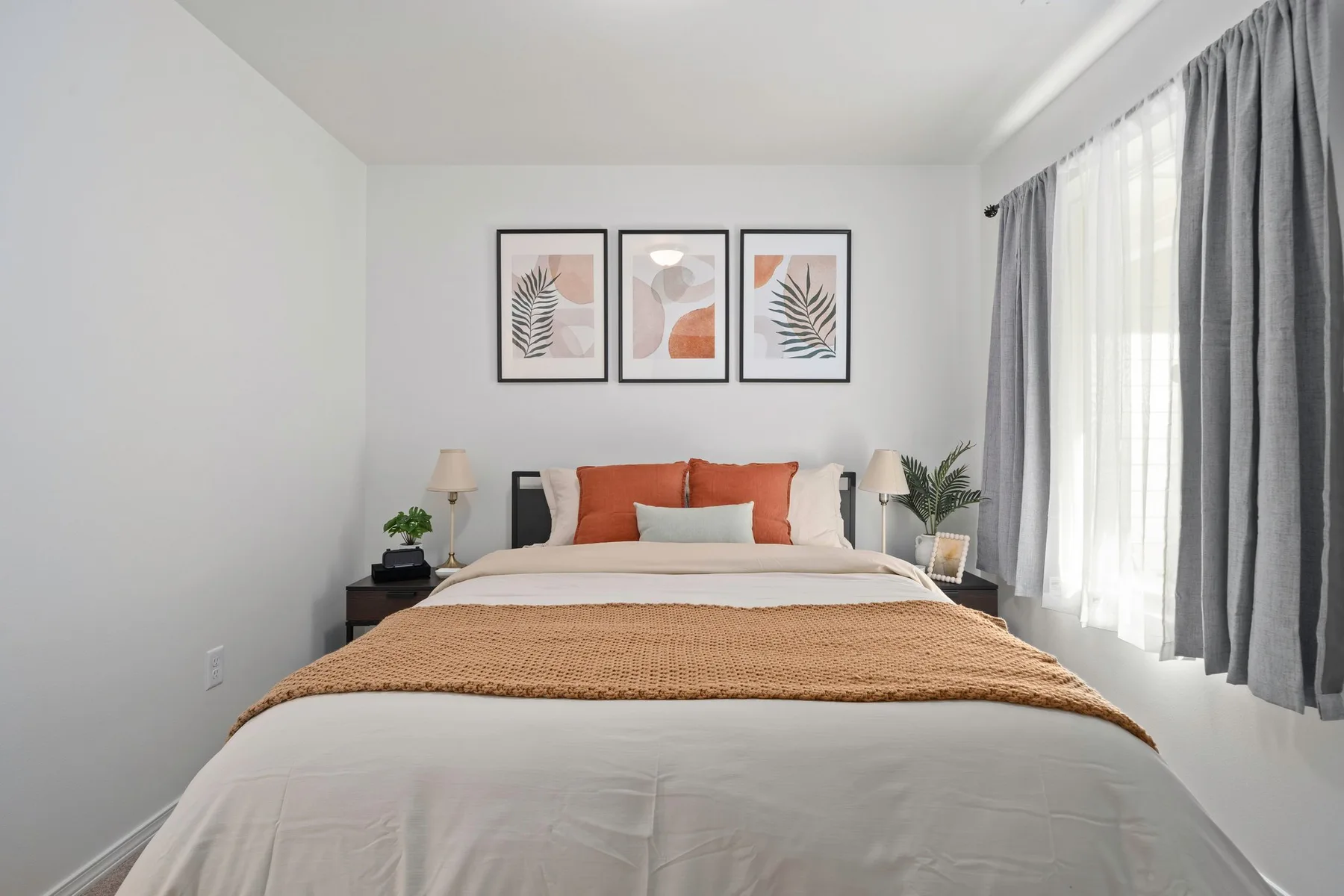 Un dormitorio luminoso con una cama bien tendida y cuadros enmarcados encima.