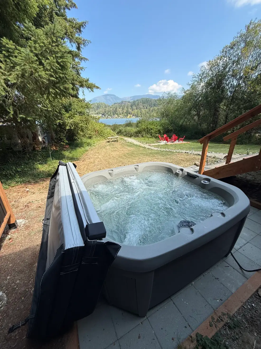 Una bañera de hidromasaje al aire libre está en un patio con vistas a un lago y colinas boscosas.
