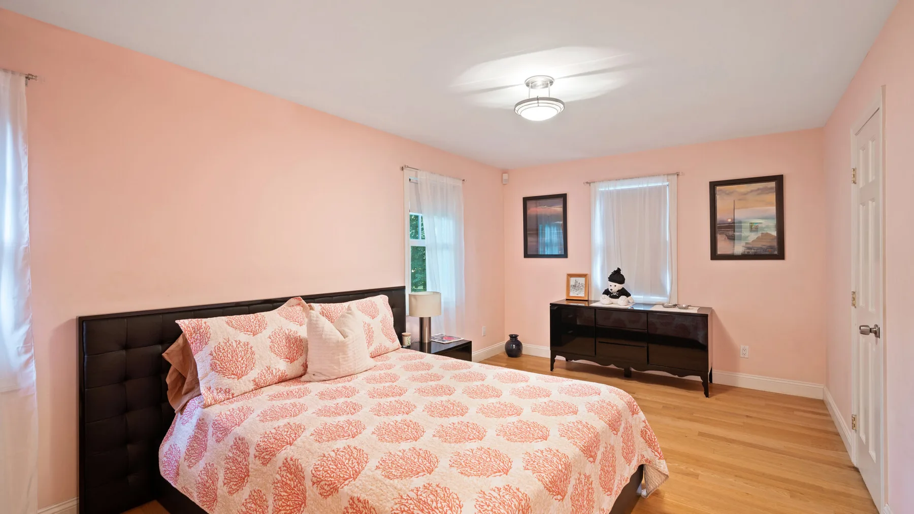 A bedroom with a bed, pink patterned bedding, and a dark dresser.