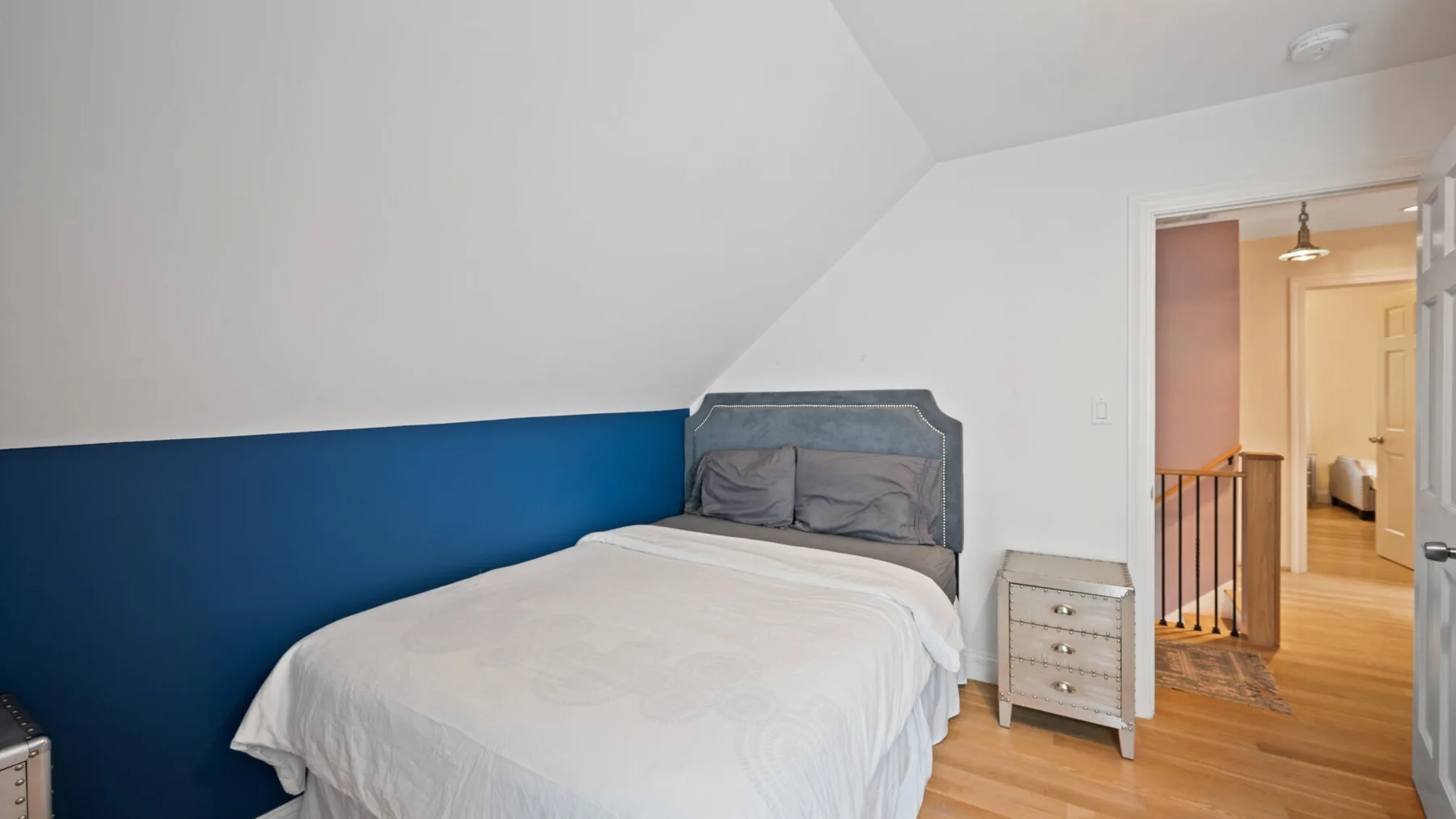 A bedroom with a bed beside a blue accent wall and a doorway to the hall.
