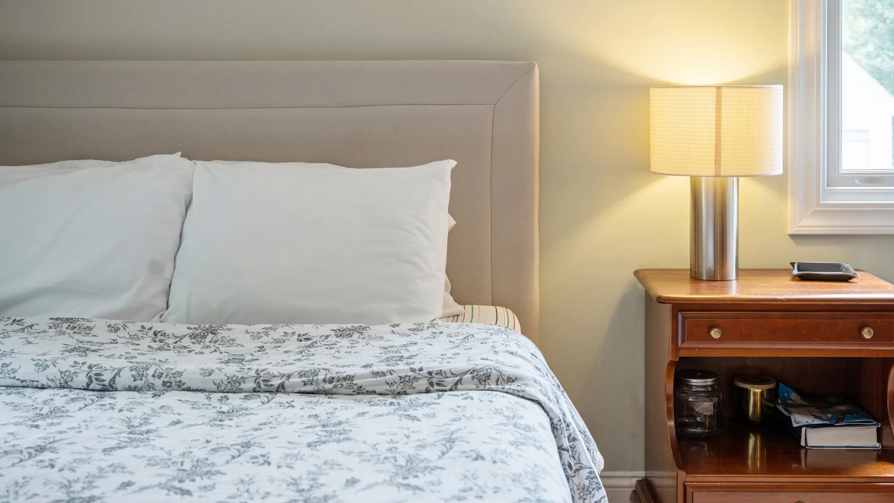 A bedroom with a neatly made bed and a lit bedside lamp.