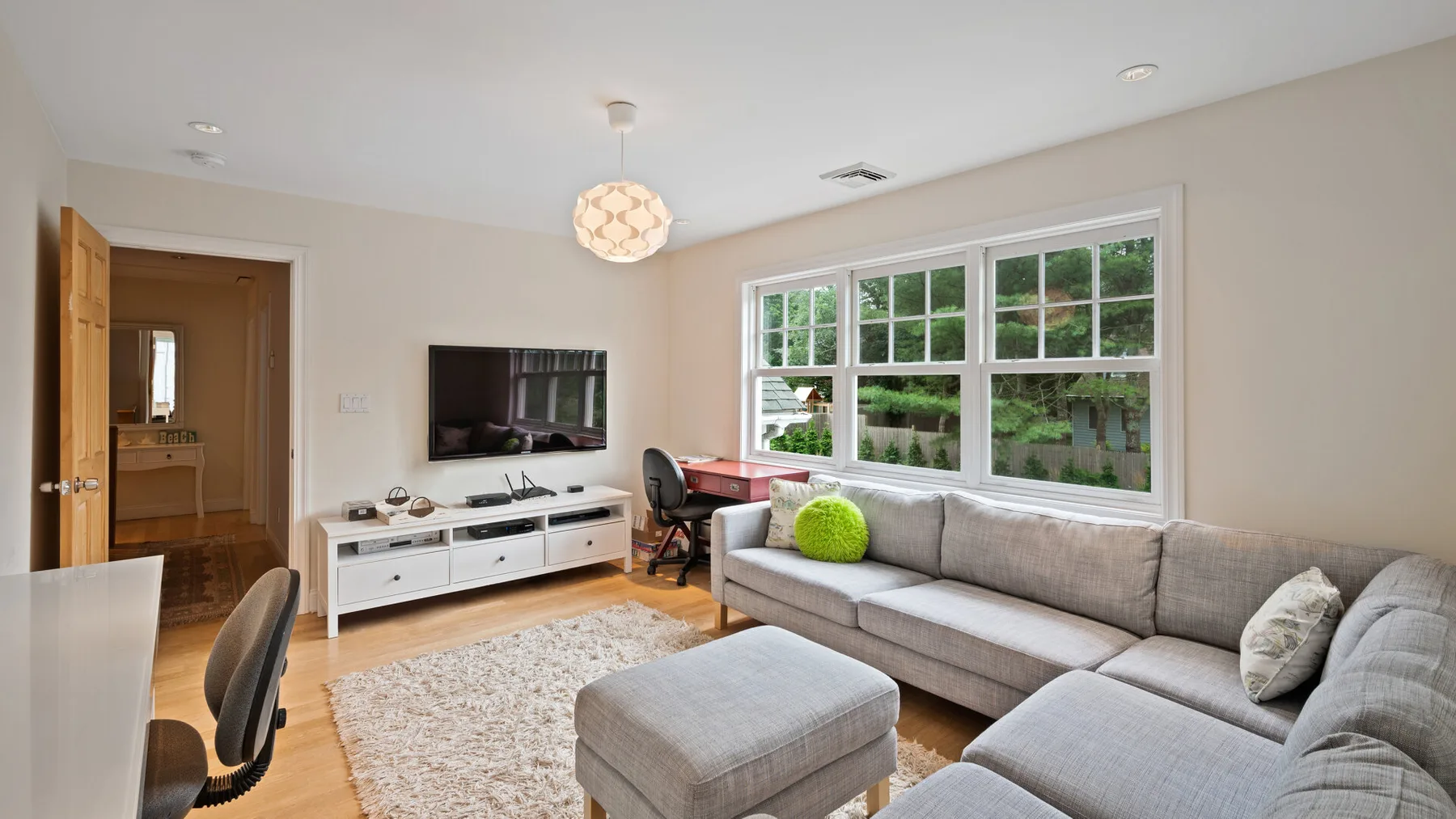 A living room with a gray sectional, television, and large windows.