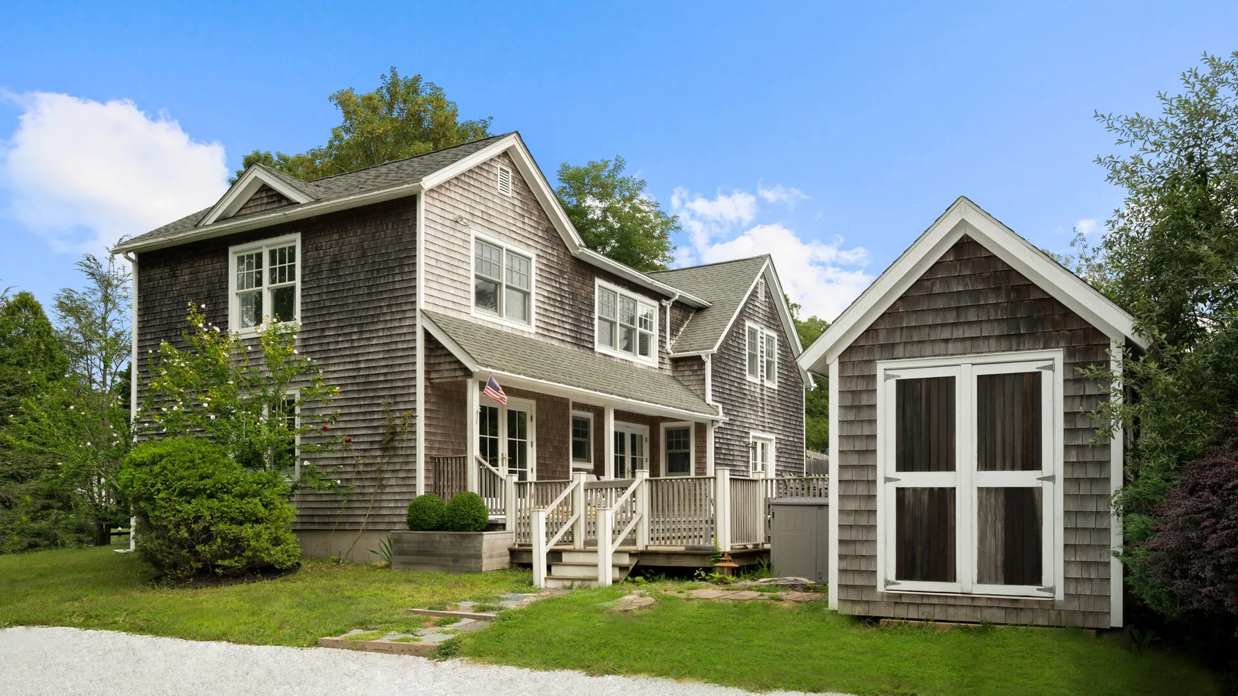 A large gray house and a small matching outbuilding stand beside a lawn.