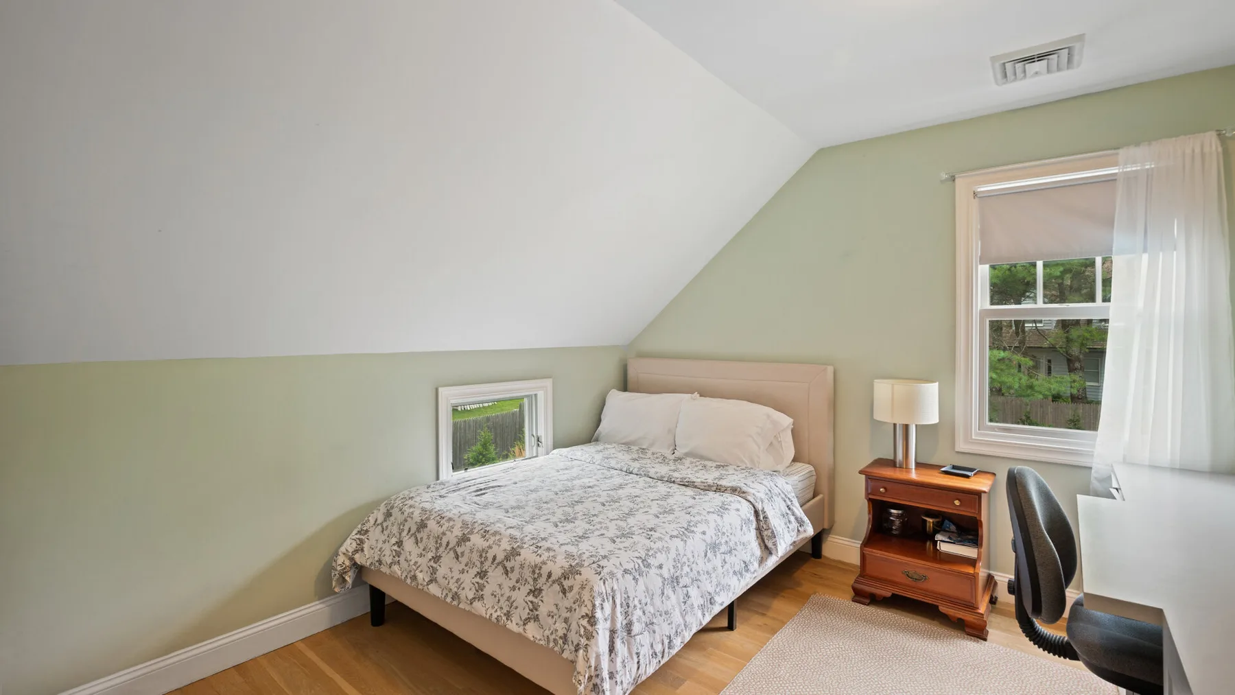 A bedroom with a bed, a small bedside table, and a window with curtains.