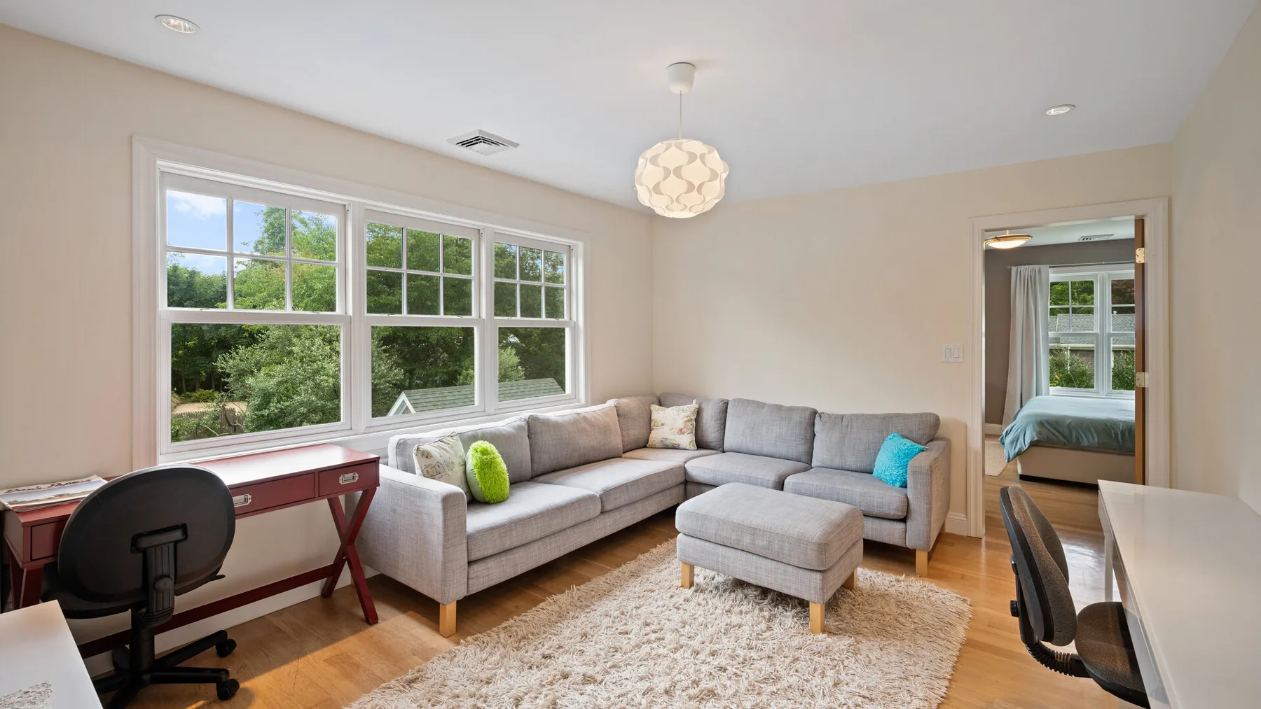 A bright living room with a sectional sofa, ottoman, and large windows.