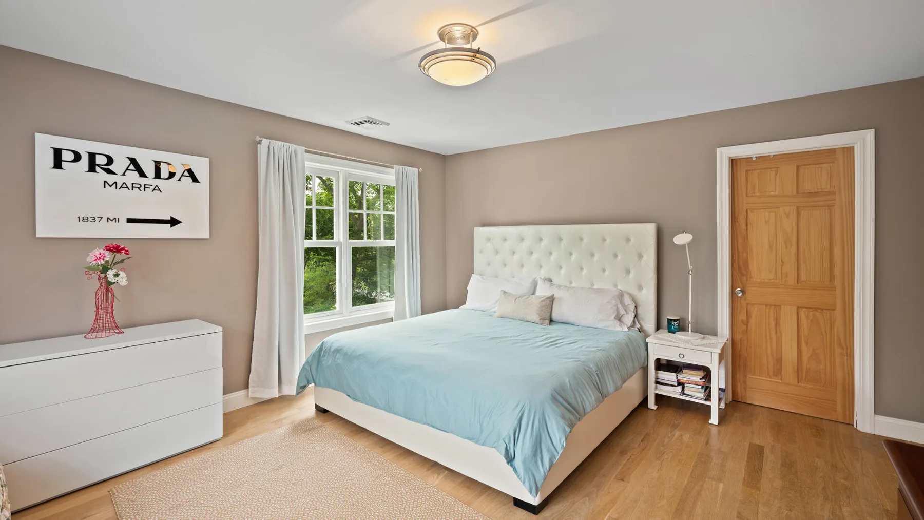 A bedroom with a bed dressed in pale blue bedding and a large window.