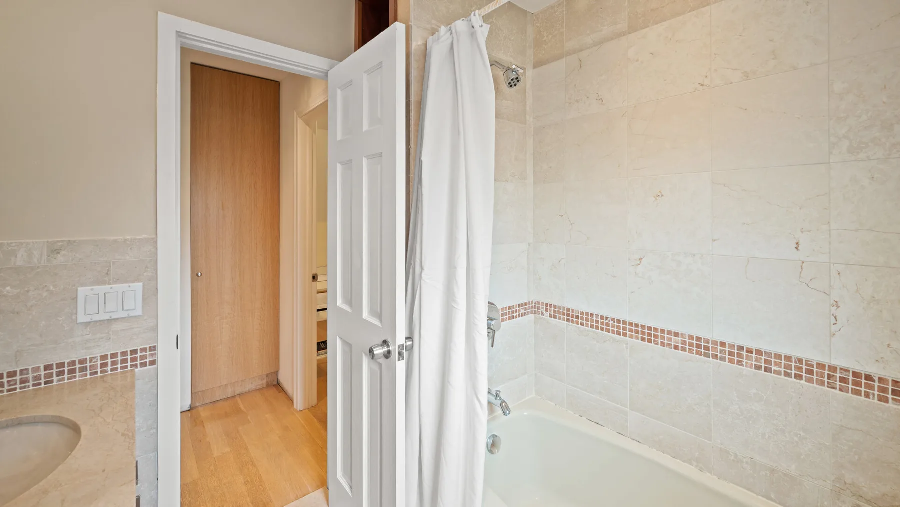 A tiled bathroom with a bathtub, shower curtain, and open doorway.