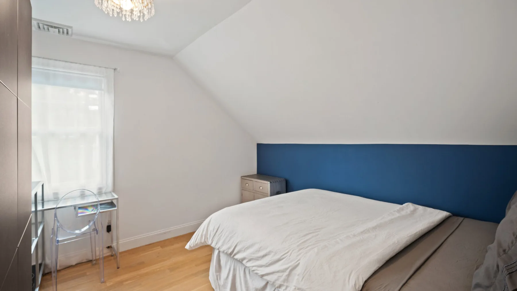 A bedroom with a bed, blue headboard, and window-side desk.