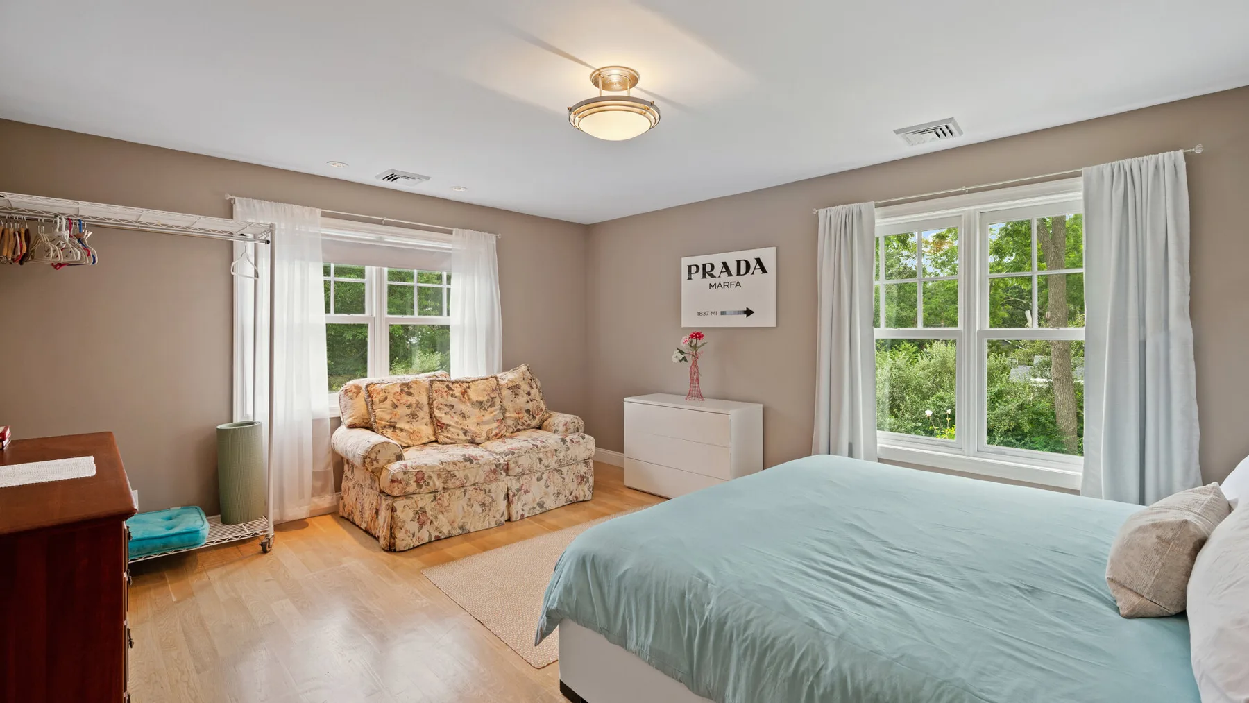 A bedroom with a bed, a floral sofa, and windows overlooking greenery.