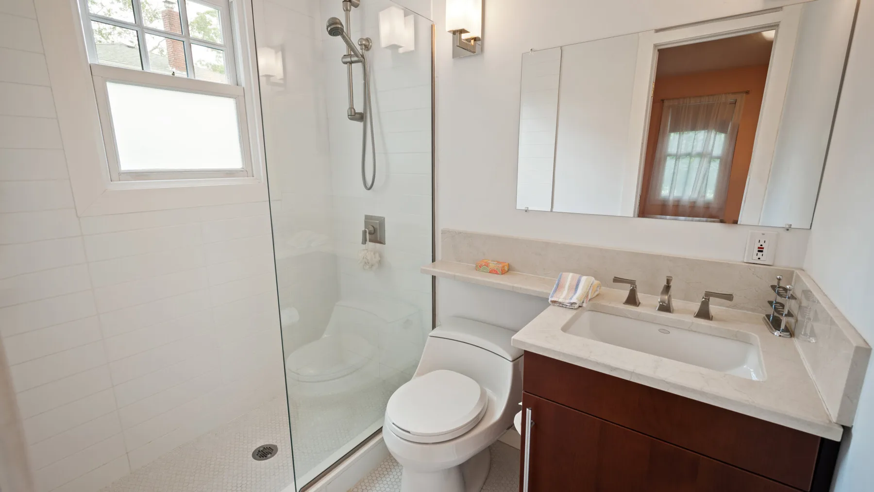 A bright bathroom with a shower, toilet, and sink beneath a wide mirror.