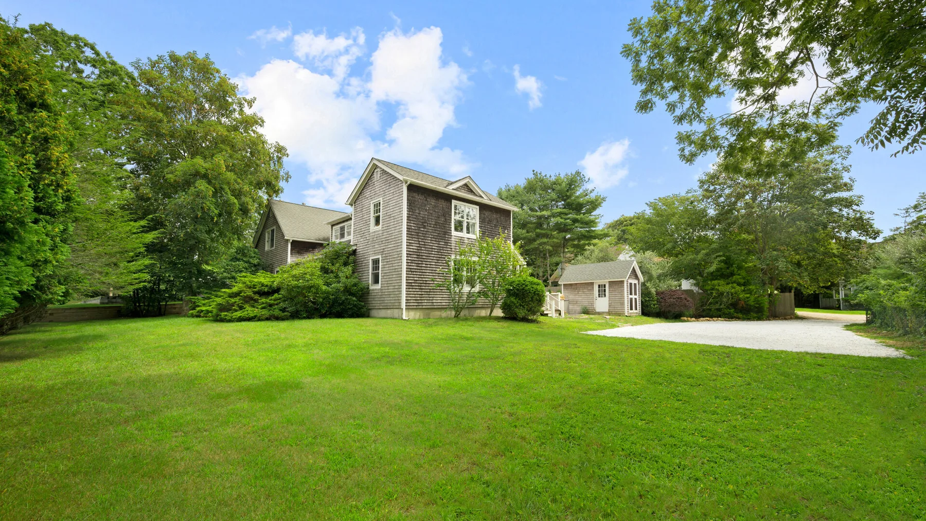 A large house and a smaller outbuilding sit beside a broad green lawn.