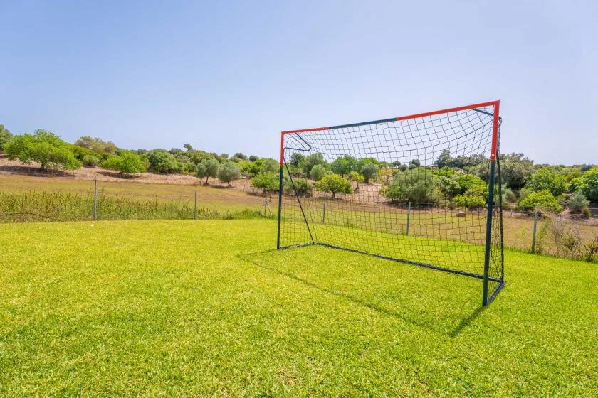 A soccer goal stands on a grassy field with trees in the background.