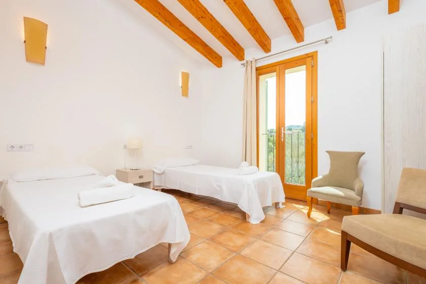 A bright bedroom with two beds and a glass door opening onto a balcony.