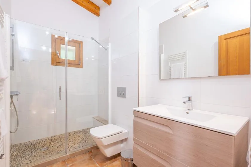 A bright bathroom with a glass shower, toilet, and vanity.